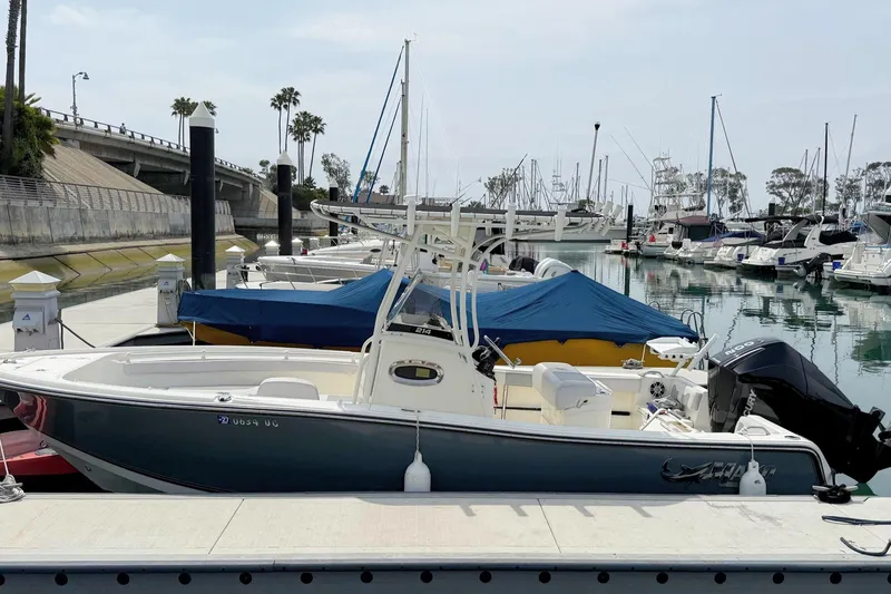 Slide: The Image of 2024 Mako 214 Center Console boat docked in a marina with other vessels. - 1