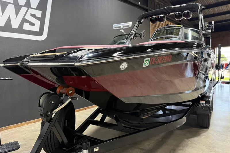 Slide: The Image of 2023 MasterCraft XStar S boat on trailer in showroom, sleek black and red design. - 20
