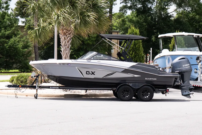 The Image of 2023 Glastron GX 210 boat on trailer, parked near palm trees. - 1