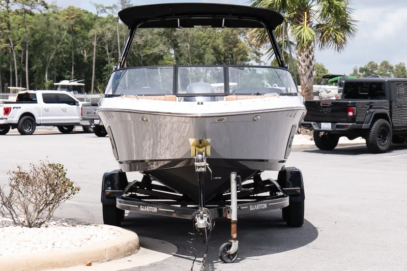 Slide: The Image of 2023 Glastron GX 210 boat on trailer in parking lot, surrounded by trees and vehicles. - 3