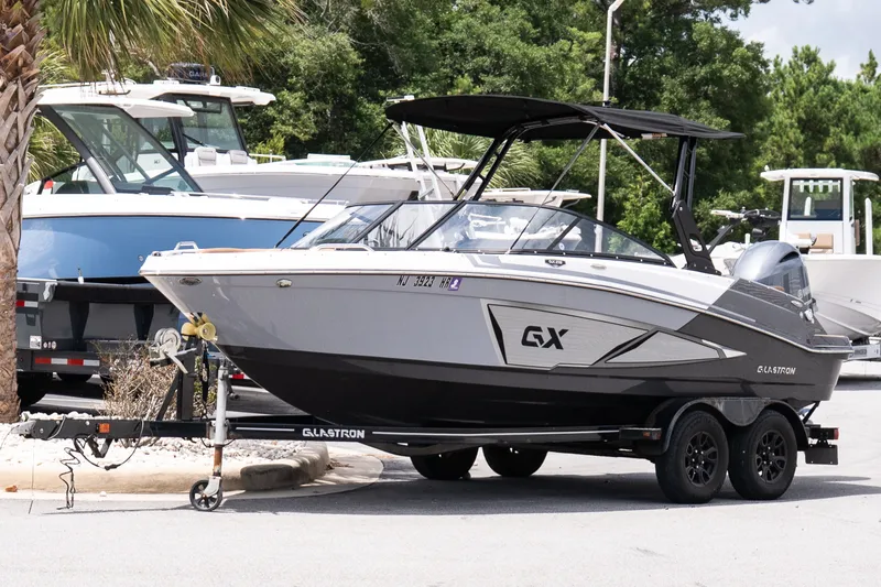 Slide: The Image of 2023 Glastron GX 210 boat on trailer, parked outdoors with other boats nearby. - 2