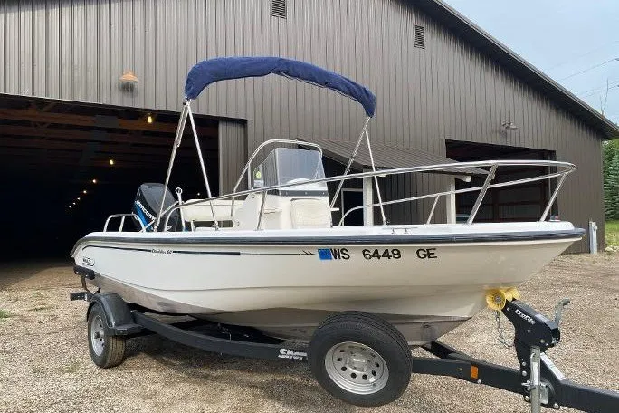 The Image of 2002 Boston Whaler 180 Dauntless boat on trailer, parked outside a large garage. - 0