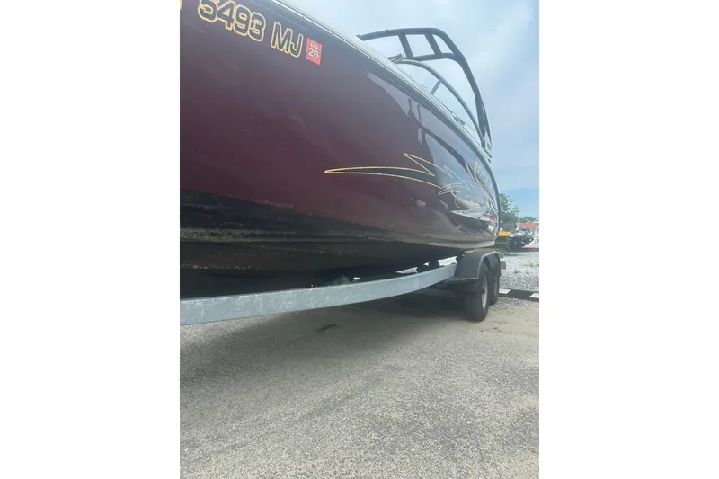 Slide: The Image of 2023 Yamaha Boats 252S on trailer, maroon hull with gold accents, parked outdoors. - 16