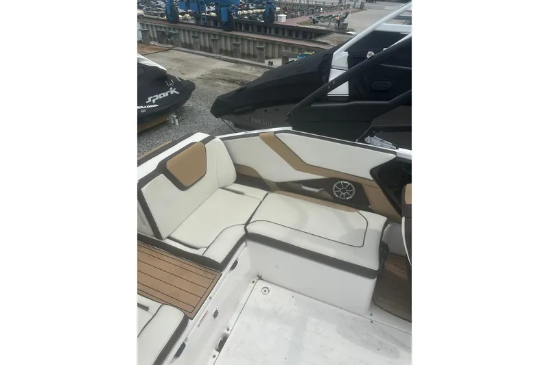 Slide: The Image of 2023 Yamaha Boats 252S interior with white and tan seating, docked near jet skis. - 34