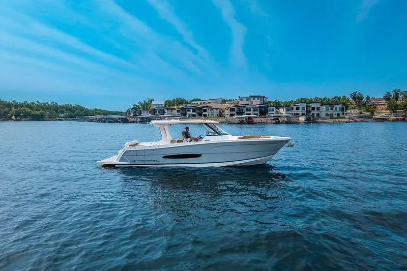 The Image of 2026 Regal 38 Surf boat cruising on a serene lake under a clear blue sky. - 0