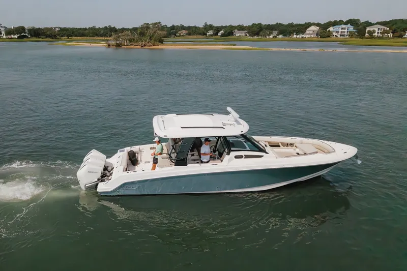Slide: The Image of 2023 Boston Whaler 350 Realm cruising on a serene lake with scenic background. - 19