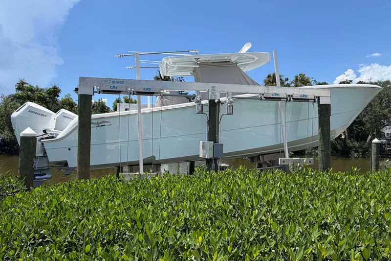 The Image of 2024 Invincible 33 Catamaran on lift, featuring twin Mercury engines, surrounded by lush greenery. - 0
