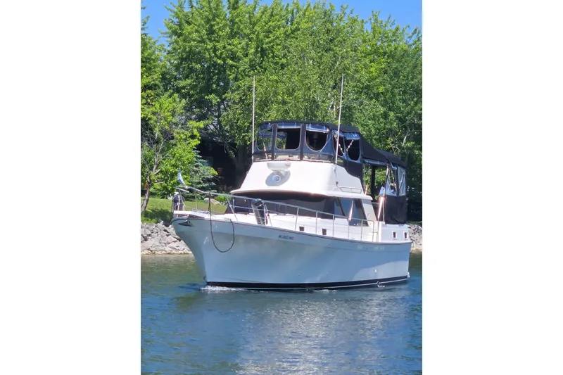 The Image of 1988 Mainship 36 Double Cabin yacht on a serene lake with lush greenery. - 1