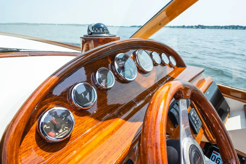 Slide: The Image of 2008 Hinckley Talaria 29R dashboard with wooden finish, gauges, and steering wheel on open water. - 24