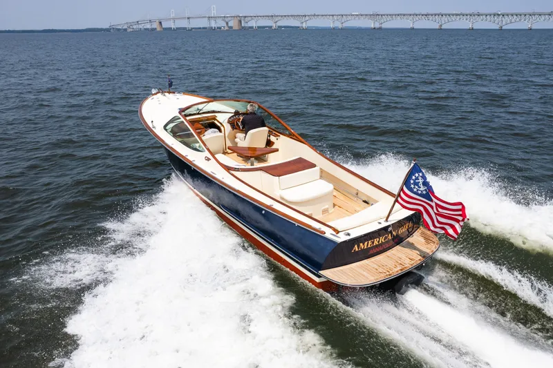 Slide: The Image of 2008 Hinckley Talaria 29R cruising on water, American flag waving, bridge in background. - 5