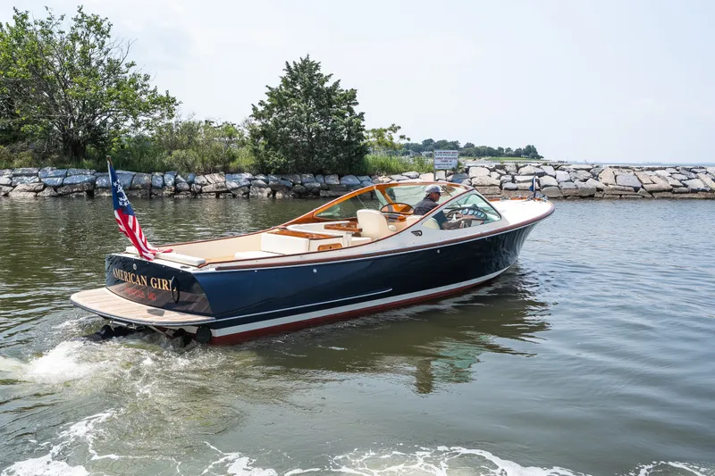Slide: The Image of 2008 Hinckley Talaria 29R cruising on a calm waterway, featuring elegant design and American flag. - 16