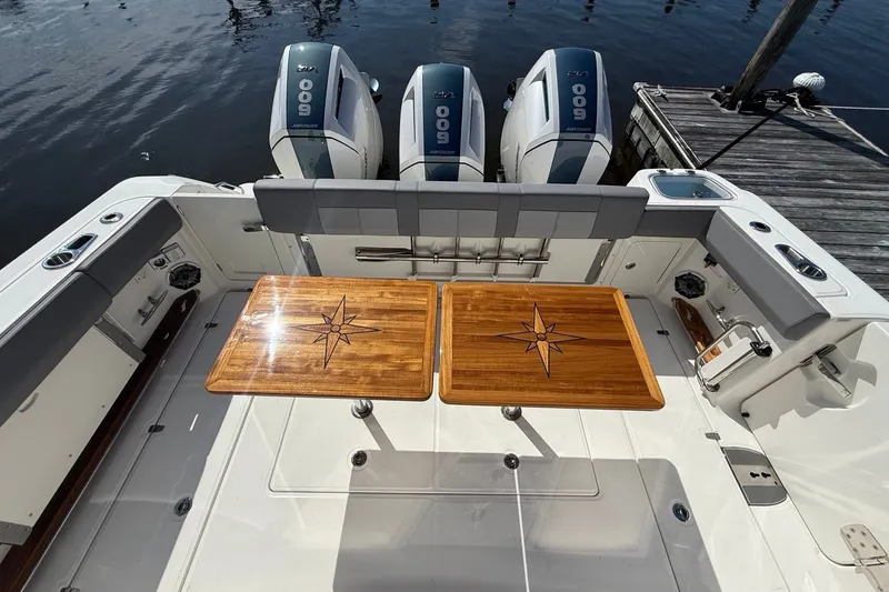 Slide: The Image of 2024 Boston Whaler 420 Outrage boat deck with wooden tables and triple outboard engines. - 18