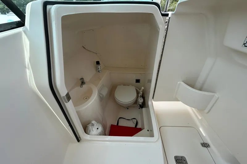 Slide: The Image of Interior of 2012 Pursuit DC 265 Dual Console boat's compact bathroom with toilet and sink. - 16