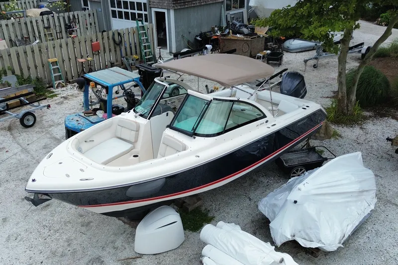 Slide: The Image of 2012 Pursuit DC 265 Dual Console boat in a yard, surrounded by equipment and trees. - 5