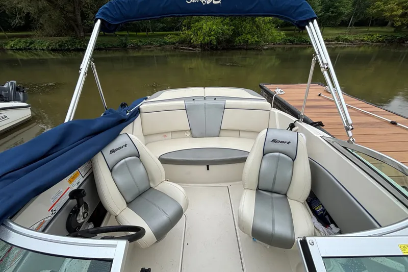 Slide: The Image of 2010 Sea Ray 185 Sport boat interior with seating and steering wheel, docked by a river. - 4