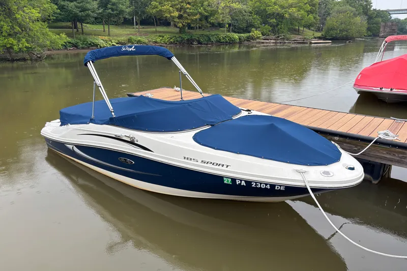 The Image of 2010 Sea Ray 185 Sport boat docked on a calm river with blue covers. - 0