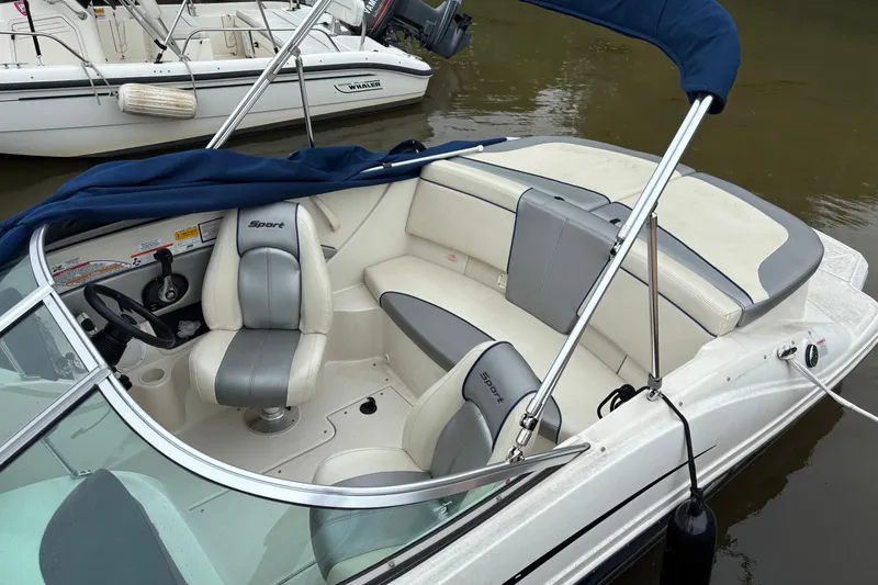 Slide: The Image of 2010 Sea Ray 185 Sport boat interior with seating and steering wheel, docked on calm water. - 2
