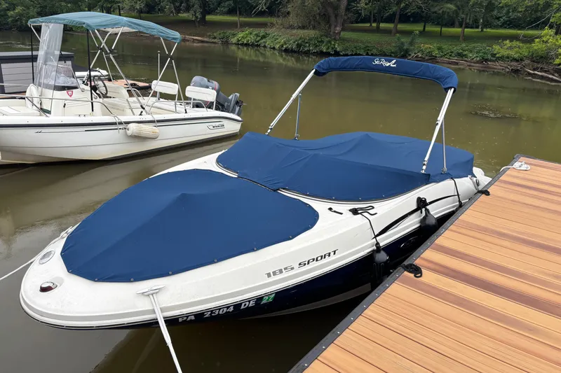 Slide: The Image of 2010 Sea Ray 185 Sport boat docked with blue cover on a calm river. - 1