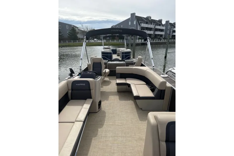 Slide: The Image of 2025 Harris Cruiser 230 pontoon boat with spacious seating, docked by waterfront homes. - 7