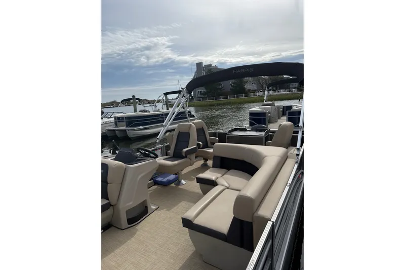 Slide: The Image of 2025 Harris Cruiser 230 pontoon boat with spacious seating, docked by a serene waterfront. - 9