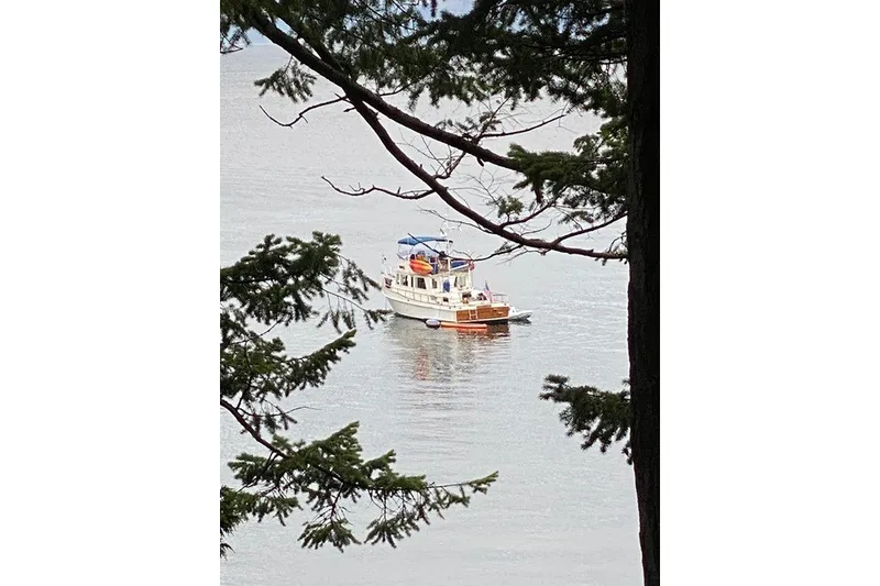 Slide: The Image of 1988 Grand Banks 42 Classic yacht on calm water, framed by tree branches. - 86