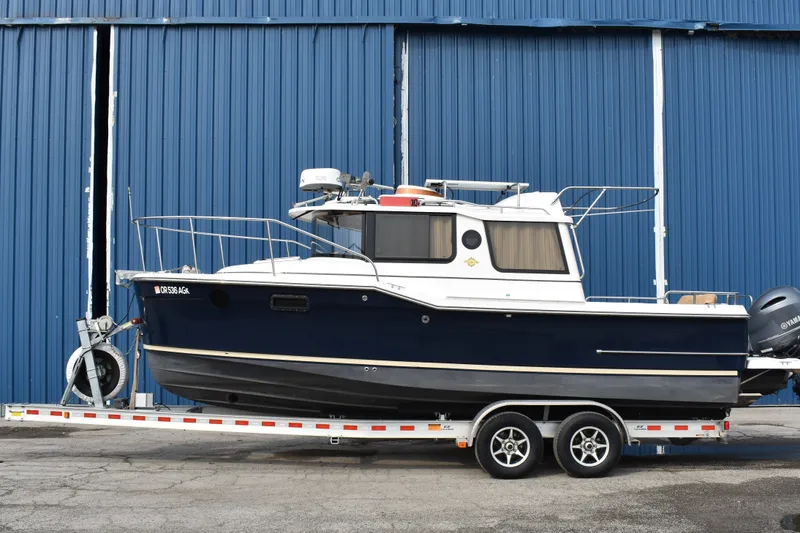 The Image of 2019 Ranger Tugs R-23 boat on trailer, parked by a blue warehouse. - 0