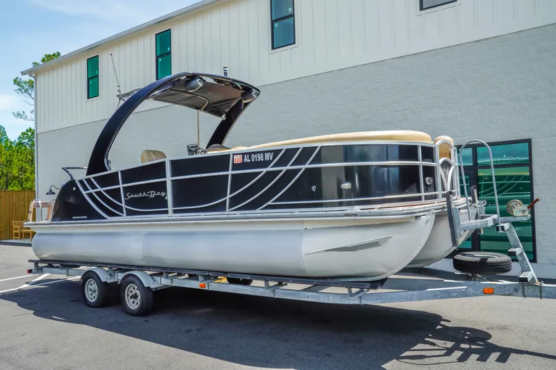 The Image of 2016 South Bay 724 SPORT DLX pontoon boat on trailer, parked outside a building. - 1