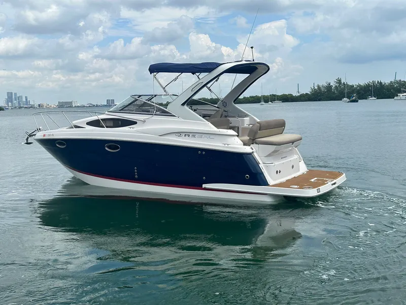 Slide: The Image of A 2014 Regal 30 Express boat on calm water with a city skyline in the background. - 12