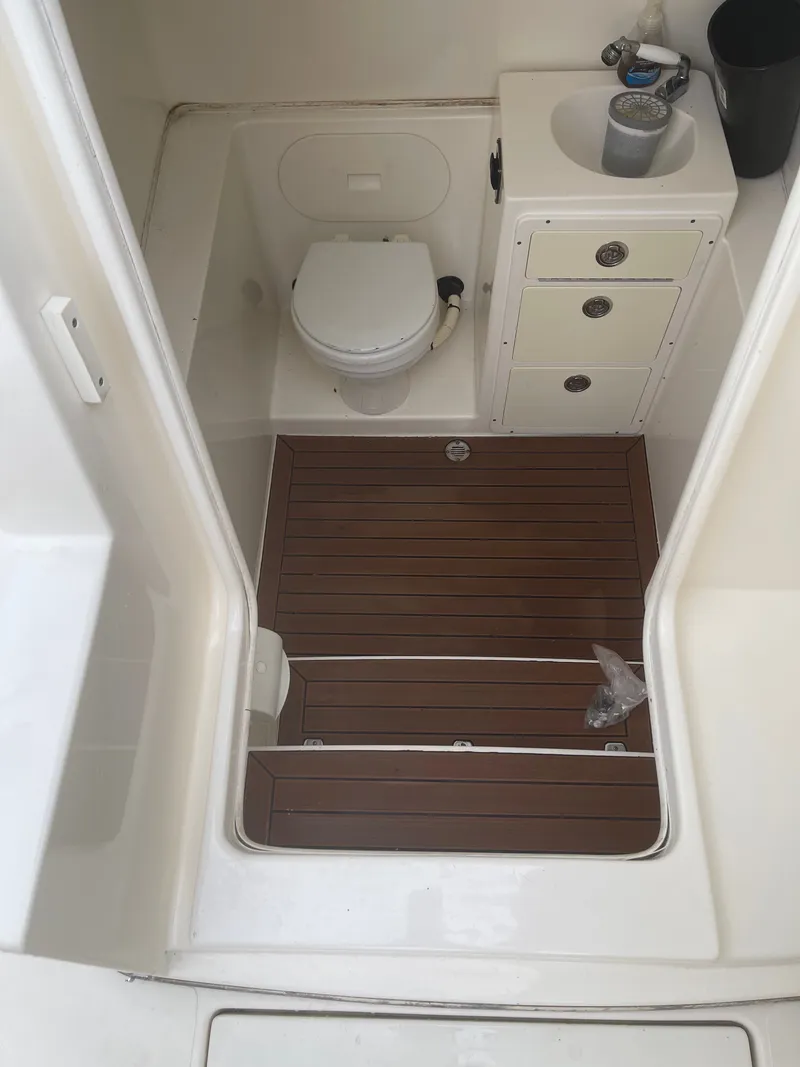 Slide: The Image of The image shows a boat toilet with wooden flooring, a sink, and drawers. - 28