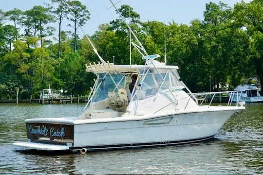 The Image of 1998 Pursuit 3000 Offshore boat on a calm river with lush green trees. - 1