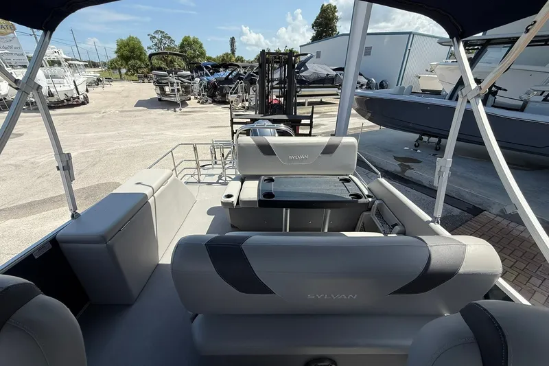 Slide: The Image of 2022 Sylvan L3 DLZ pontoon boat interior with seating and table, parked in a marina. - 12