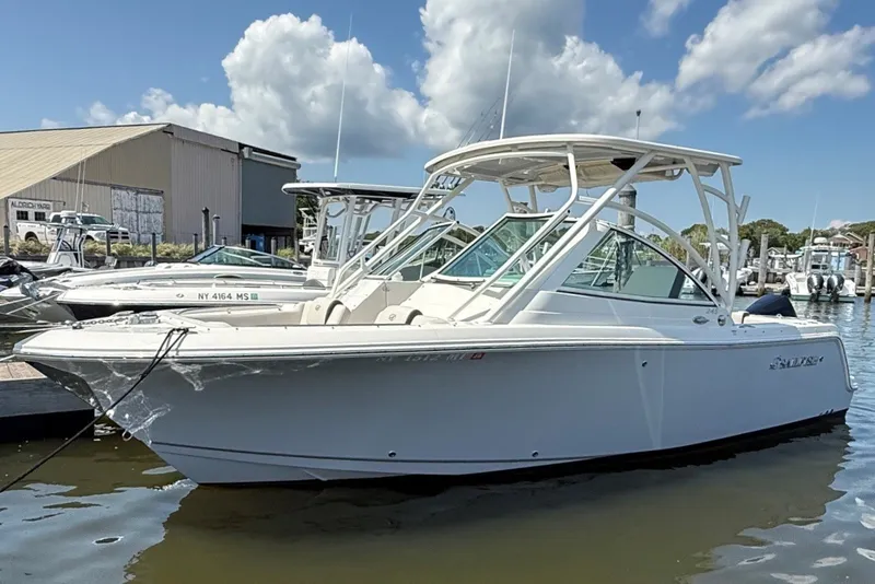 The Image of A 2022 Sailfish 245 DC is docked in the water, surrounded by other boats and a building in the background. - 0