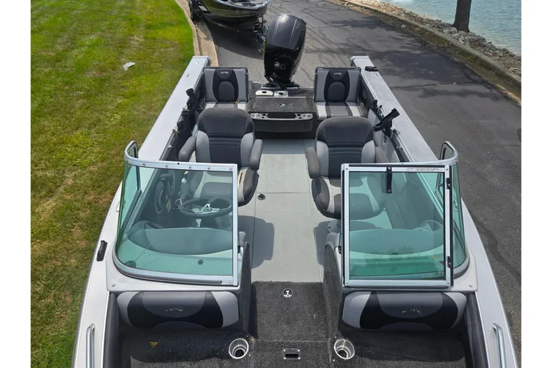 Slide: The Image of 2014 Lund 1900 Tyee boat interior with seating and windshield, parked near water. - 24