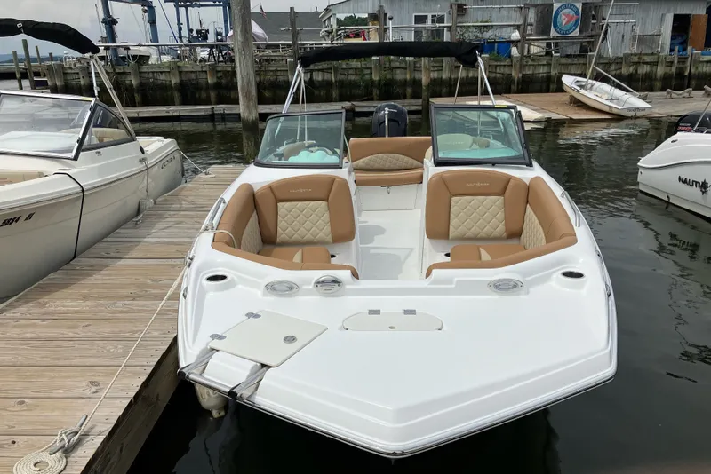 Slide: The Image of 2025 NauticStar 223 DC Deck boat docked, featuring tan seating and sleek design. - 3