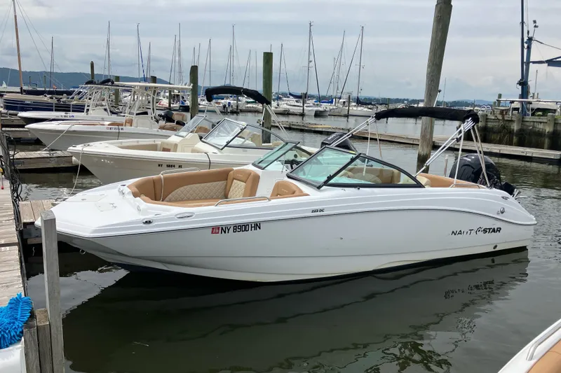 Slide: The Image of 2025 NauticStar 223 DC Deck boat docked at a marina, featuring sleek design and spacious seating. - 2