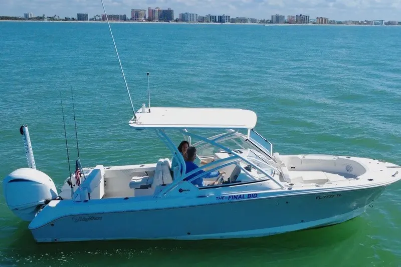 Slide: The Image of 2023 Edgewater 248CX Crossover boat cruising on clear blue water near a city skyline. - 14