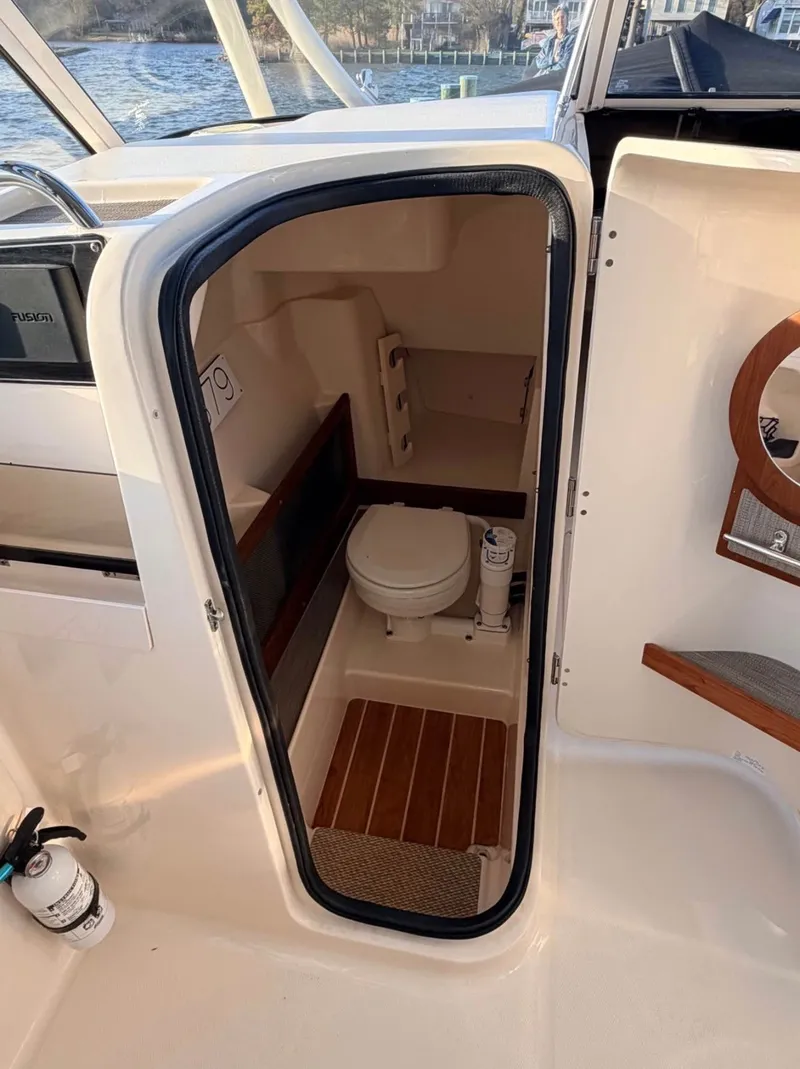 Slide: The Image of The image shows the interior of a 2022 Grady-White Freedom 275. There's a small toilet with wooden flooring and a sink. - 8