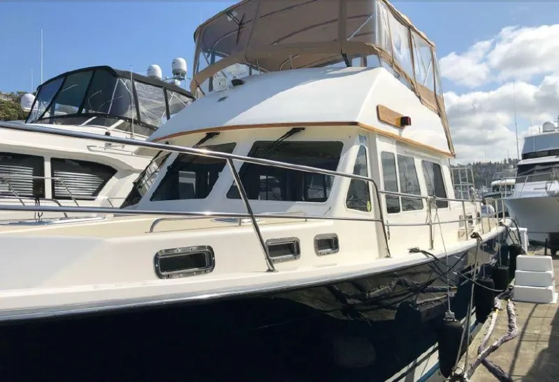 Slide: The Image of A 2000 Sabreline 47 docked in a marina, featuring an elevated pilothouse and beige canopy. - 3