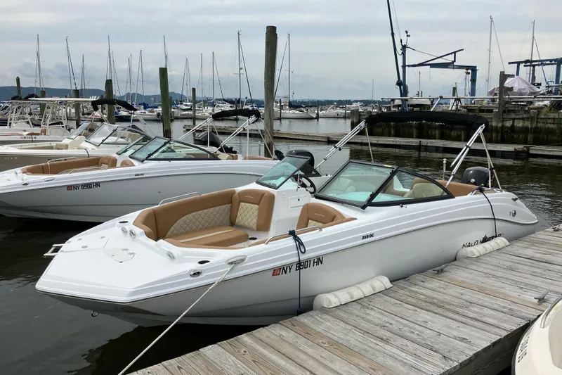 The Image of 2025 NauticStar 223 DC Deck boat docked at marina, featuring sleek design and comfortable seating. - 1
