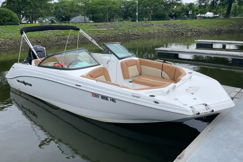 The Image of 2025 NauticStar 223 DC Deck boat docked on calm water, featuring sleek design and tan seating. - 1
