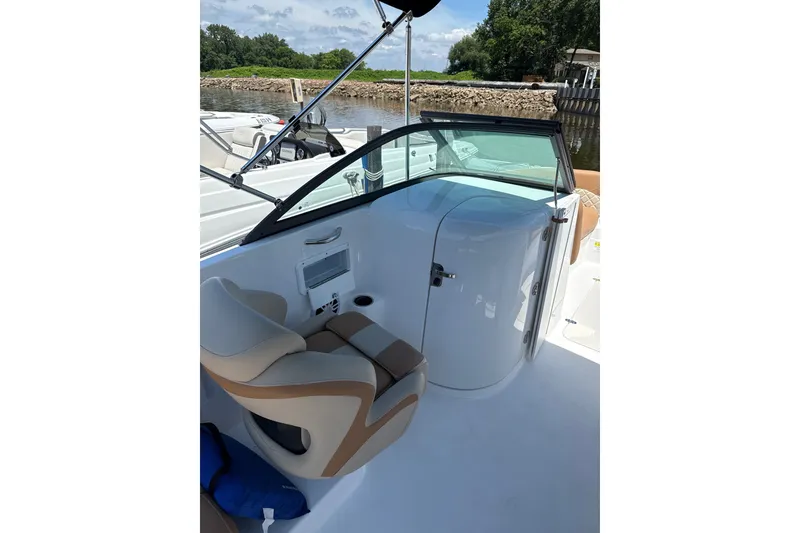 Slide: The Image of 2025 NauticStar 223 DC Deck boat interior with seating and helm, docked by a scenic river. - 7