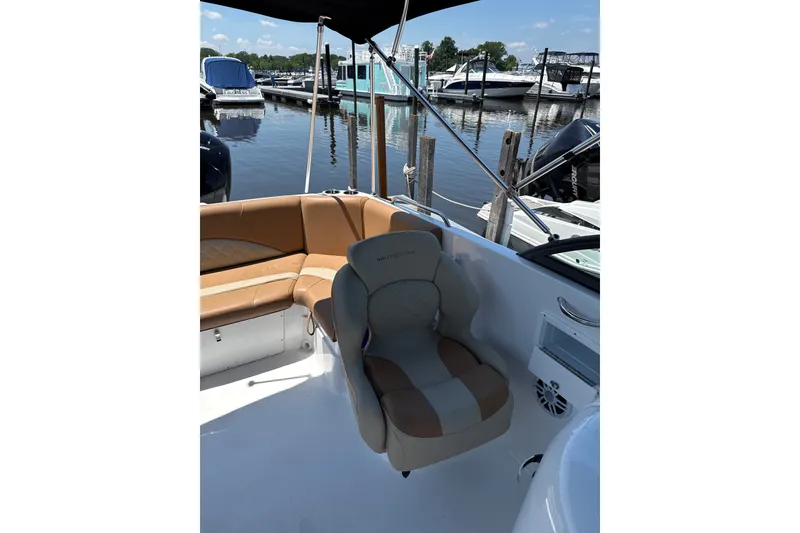 Slide: The Image of 2025 NauticStar 223 DC Deck boat interior with tan seating at marina. - 8