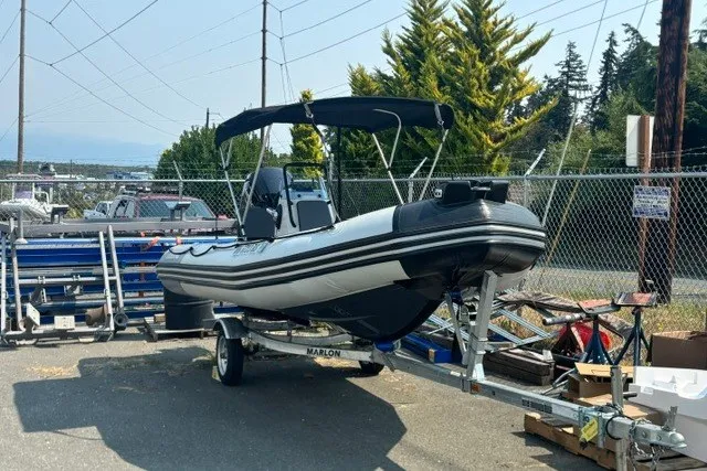 Slide: The Image of 2024 Zodiac Open 4.8 boat on trailer, parked outdoors near fencing and trees. - 4