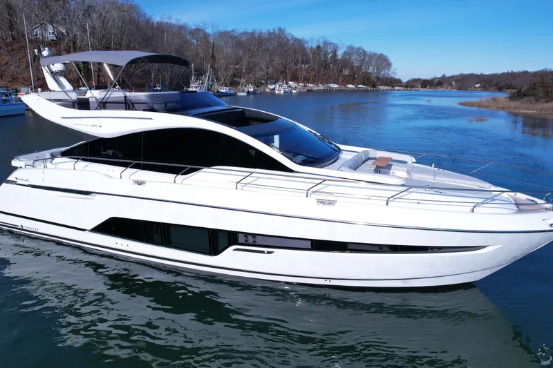 Slide: The Image of 2024 Fairline Phantom 65 yacht cruising on a serene river under a clear blue sky. - 2