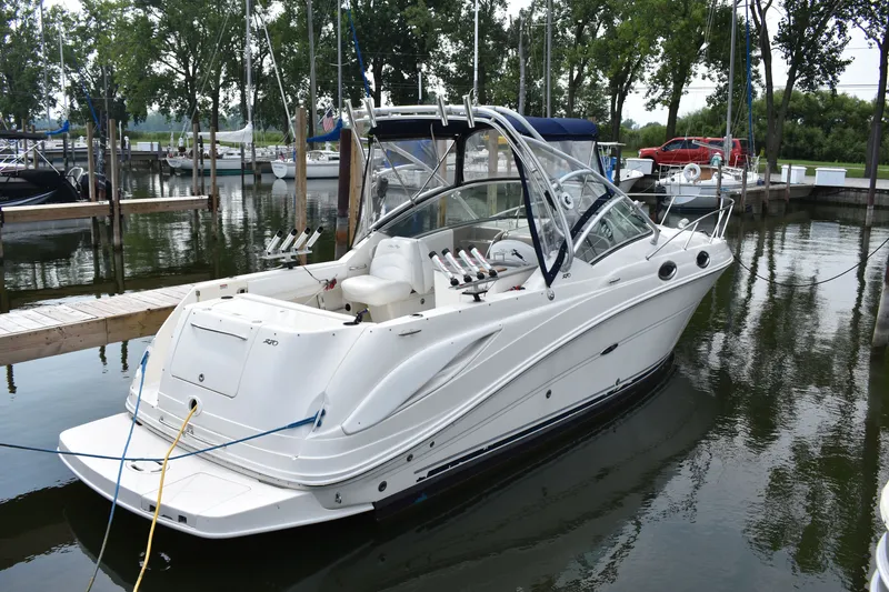 The Image of 2007 Sea Ray 270 Amberjack boat docked at a marina, surrounded by trees and other boats. - 0