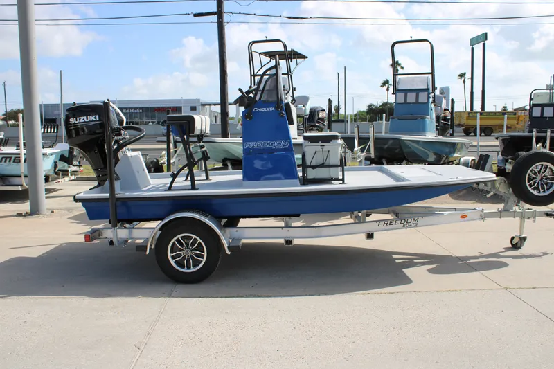 Slide: The Image of 2027 Freedom Boats Chiquita on trailer with Suzuki outboard motor, parked outdoors. - 4
