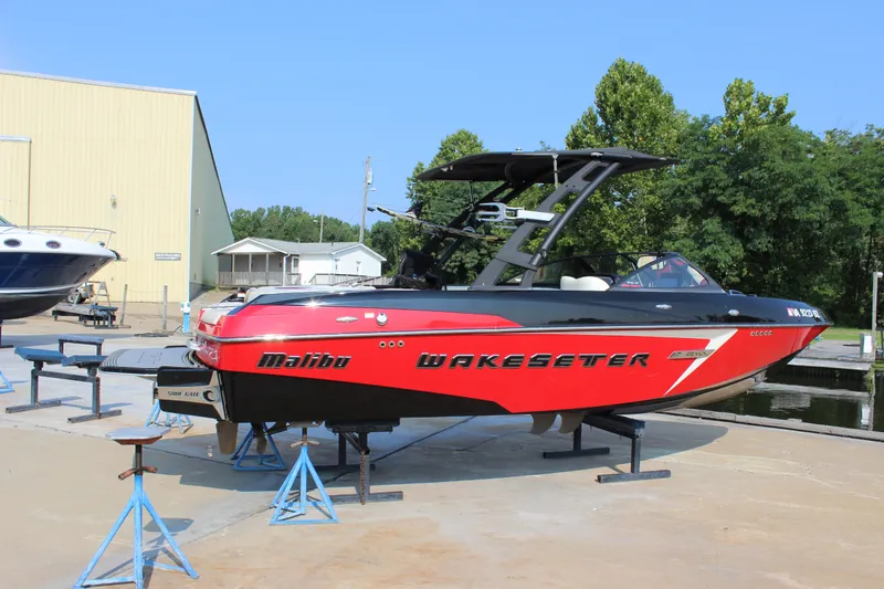 Slide: The Image of 2015 Malibu Wakesetter 22 VLX boat on stands, red and black design, outdoor setting. - 2
