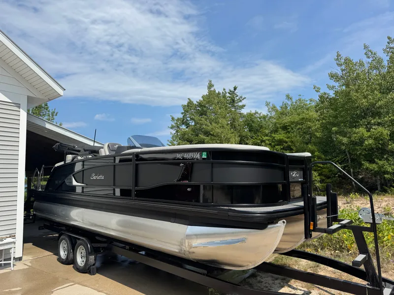 Slide: The Image of A 2024 Barletta Lusso 23M pontoon boat on a trailer, surrounded by trees and a building. - 8