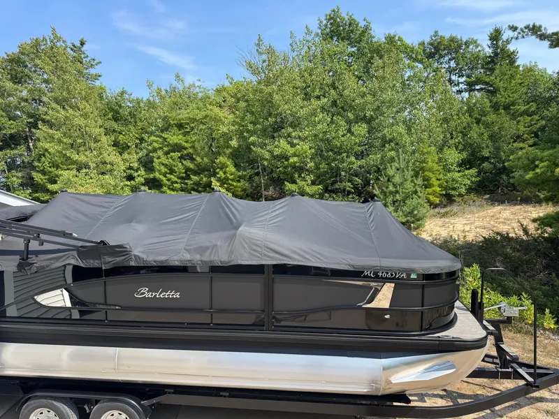 Slide: The Image of A 2024 Barletta Lusso 23M pontoon boat on a trailer, surrounded by trees. - 11