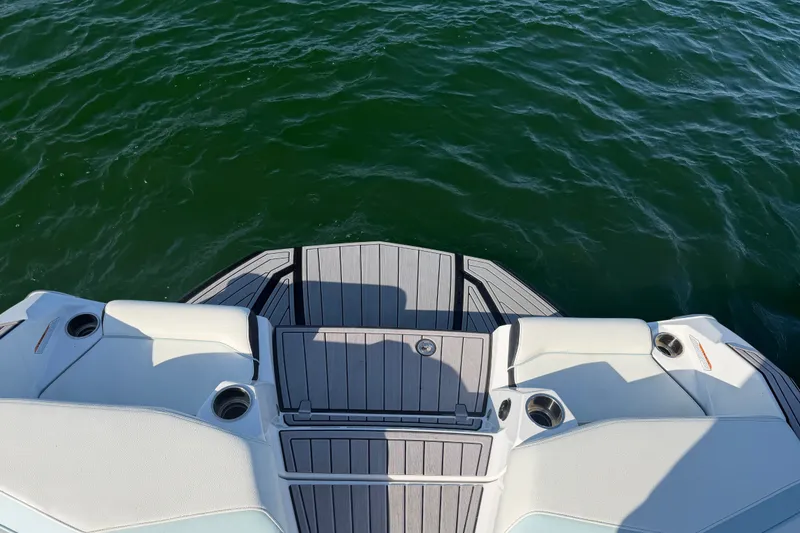 Slide: The Image of 2023 Nautique Super Air Nautique G23 boat deck on water, featuring sleek design and cup holders. - 16